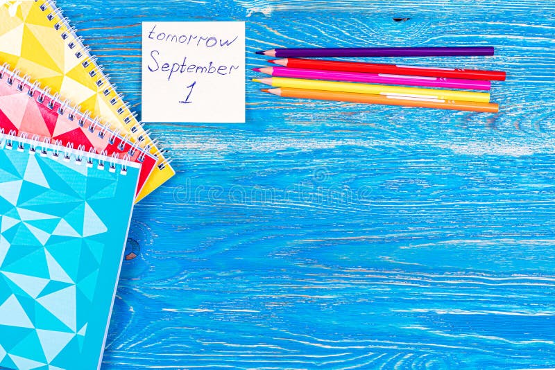 Inscription on the sticker, colored pencils and notebooks with colored covers on a wooden table. September 1. Design. Background. High quality photo. Inscription on the sticker, colored pencils and notebooks with colored covers on a wooden table. September 1. Design. Background. High quality photo