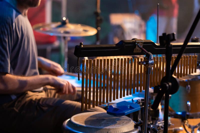 A selective  and close-up view on professional bar chimes, drums accessories, blurry view of a man playing drums in the background. A selective  and close-up view on professional bar chimes, drums accessories, blurry view of a man playing drums in the background