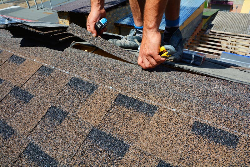 Repair of a Roofing from shingles. Roofer cutting roofing felt or bitumen during waterproofing works. Roof Shingles - Roofing. Bitumen tile roof. Repair of a Roofing from shingles. Roofer cutting roofing felt or bitumen during waterproofing works. Roof Shingles - Roofing. Bitumen tile roof.