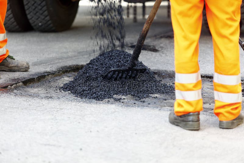 Workmen spreading asphalt to repair a pothole in a roadway. Workmen spreading asphalt to repair a pothole in a roadway.