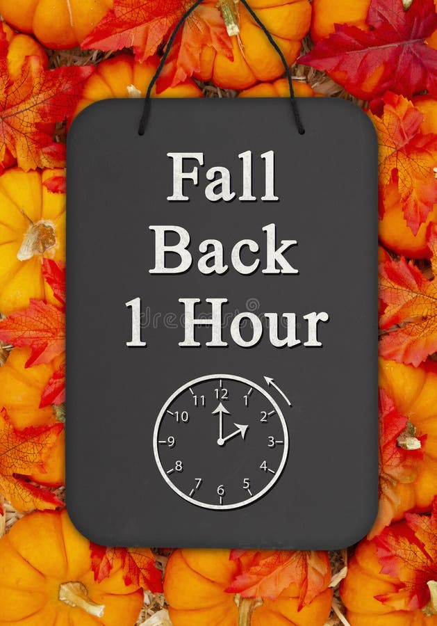 Fall Back 1 hour time change message on a chalkboard sign on pumpkins with fall leaves and a straw hay. Fall Back 1 hour time change message on a chalkboard sign on pumpkins with fall leaves and a straw hay