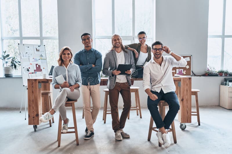 Successful professionals. Full length of young modern people in smart casual wear smiling and looking at camera while standing in the creative office. Successful professionals. Full length of young modern people in smart casual wear smiling and looking at camera while standing in the creative office