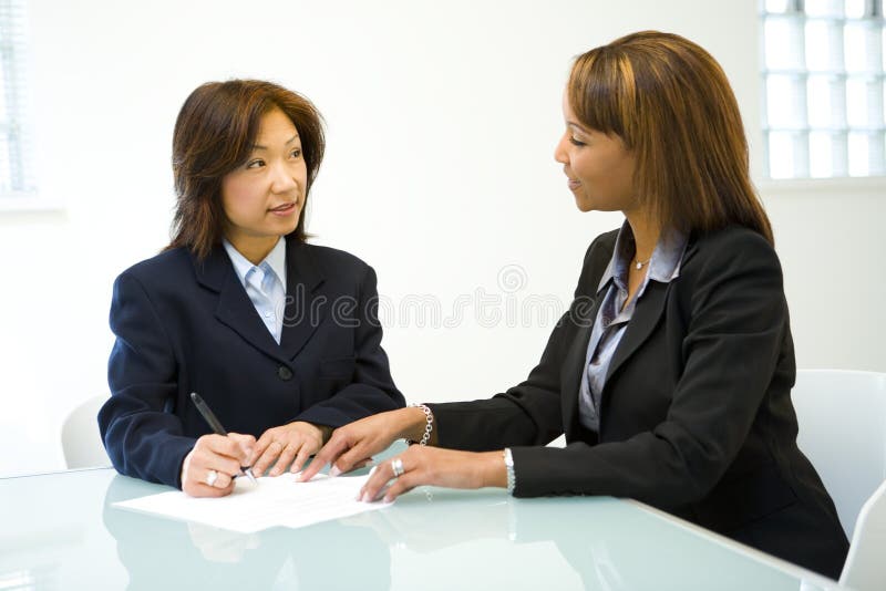 Business meeting between two women in business attire, seated at a table. Business meeting between two women in business attire, seated at a table.