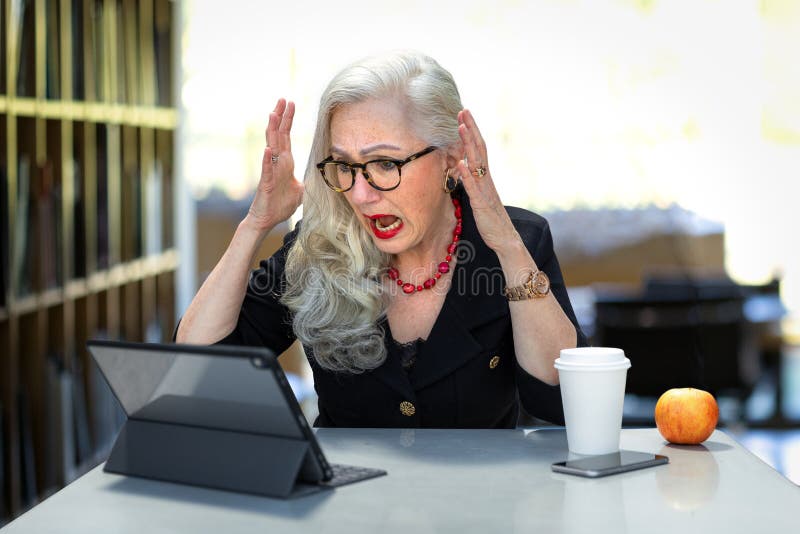 Senior business woman with stress, anxiety, overloaded on computer at the office, panicked and having an anxiety attack, stressed at work for possible taxes deadline or identity theft. Senior business woman with stress, anxiety, overloaded on computer at the office, panicked and having an anxiety attack, stressed at work for possible taxes deadline or identity theft