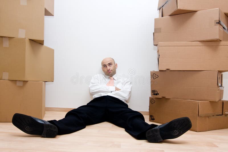 A view of a businessman resting on the floor, surrounded by high stacks of cardboard boxes. Could be beginning or just completing a task related to shipping. A view of a businessman resting on the floor, surrounded by high stacks of cardboard boxes. Could be beginning or just completing a task related to shipping.