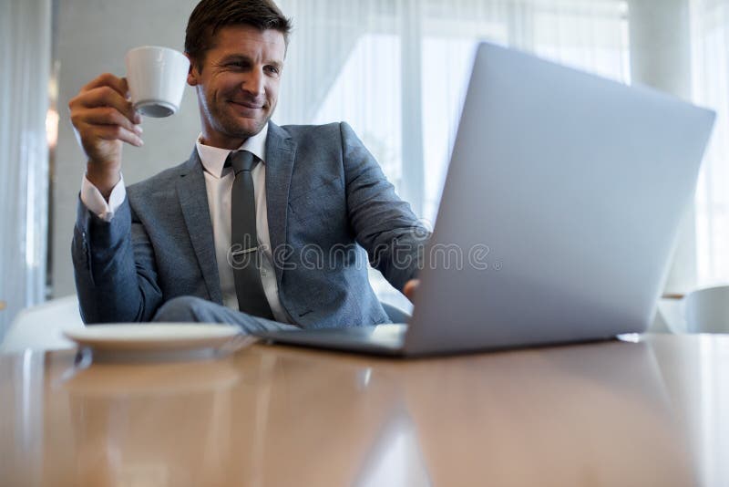 Επιχειρηματίας χρησιμοποιώντας το lap-top και έχοντας τον καφέ στο γραφείο στοκ εικόνες με δικαίωμα ελεύθερης χρήσης Επιχειρηματίας χρησιμοποιώντας το lap-top και έχοντας τον καφέ στο γραφείο στοκ εικόνες με δικαίωμα ελεύθερης χρήσης