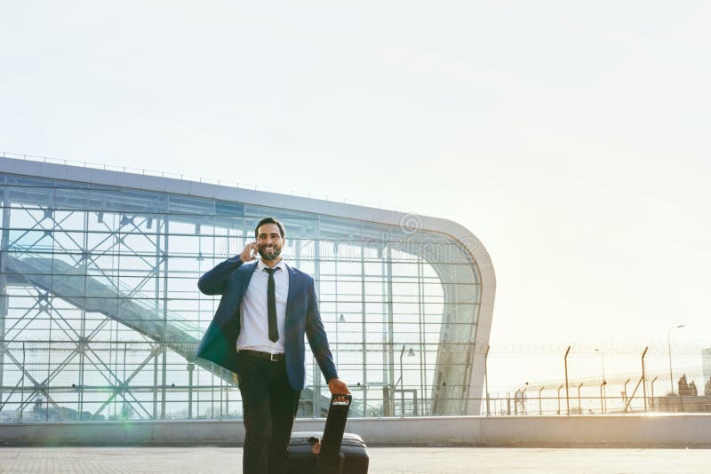 Business Man Talking On Mobile Phone Outdoors. Man With Suitcase Traveling On Business Trip. High Resolution. Business Man Talking On Mobile Phone Outdoors. Man With Suitcase Traveling On Business Trip. High Resolution