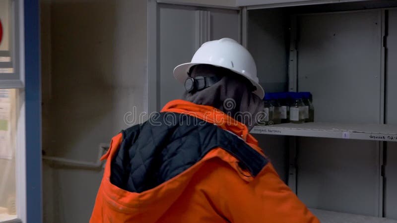 εργαζόμενος με πορτοκαλί στολή ανοίγει θήκη με υγρά χημικά φιλμ μικρού μήκους