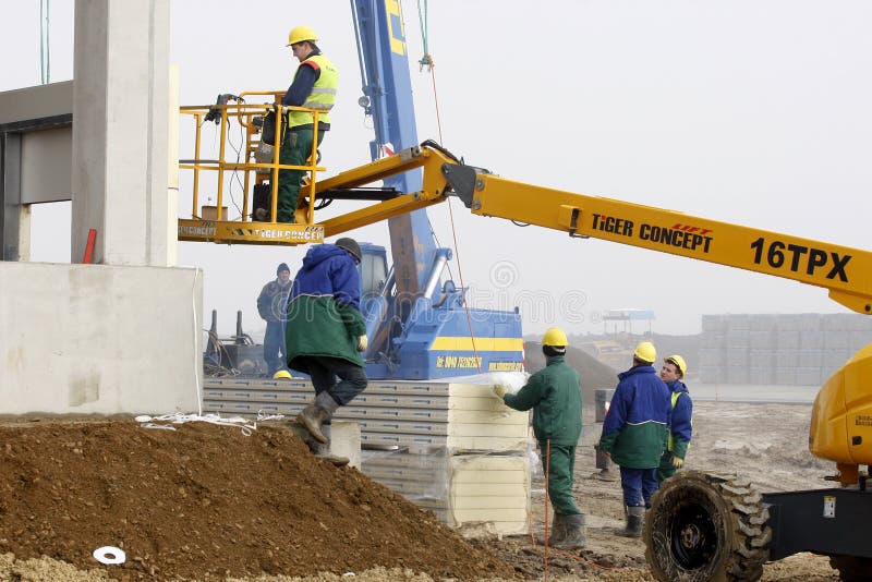 Industrial worker elevated on a cherry picker works a construction site for building a new residential block. Industrial worker elevated on a cherry picker works a construction site for building a new residential block