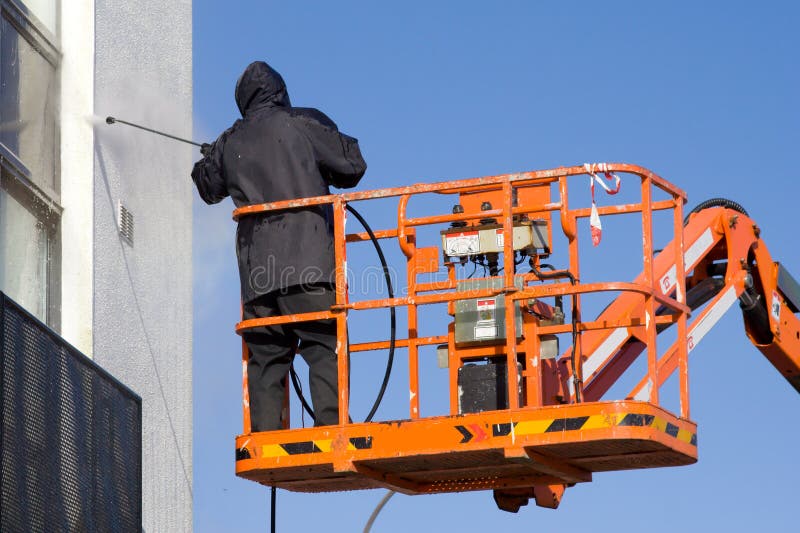 A worker washing the building staiing at the platform in a cherry-picker. A worker washing the building staiing at the platform in a cherry-picker