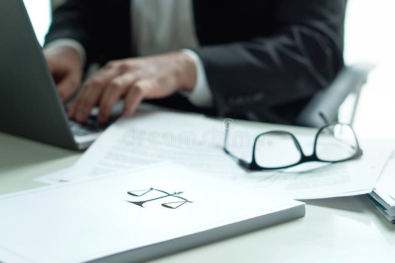 Lawyer working in office. Attorney writing a legal document with laptop computer. Glasses on table. Pile of paper with scale and justice symbol. Law firm and business concept. Lawyer working in office. Attorney writing a legal document with laptop computer. Glasses on table. Pile of paper with scale and justice symbol. Law firm and business concept.