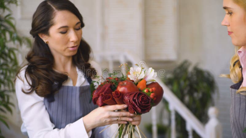 Εργασία τριών νέα όμορφη ανθοκόμων αρχιμαγείρων στο κατάστημα φρούτων λουλουδιών που κάνει την ανθοδέσμη φρούτων και λαχανικών