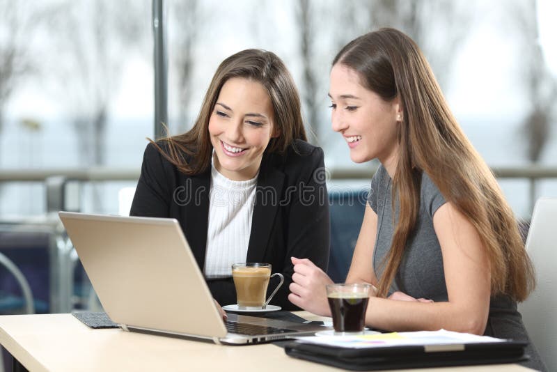 2 businesswomen working on line watching webs in a laptop in a bar with a window and and outdoors in the background. 2 businesswomen working on line watching webs in a laptop in a bar with a window and and outdoors in the background