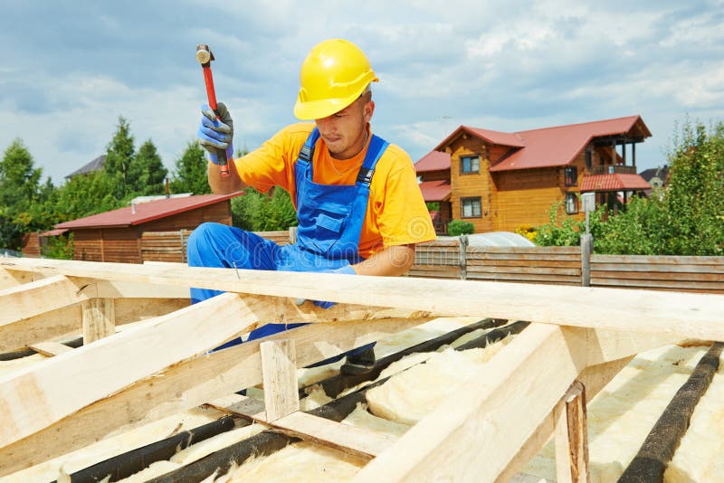 Roofer carpenter worker nailing wood board with hammer on roof installation work. Roofer carpenter worker nailing wood board with hammer on roof installation work