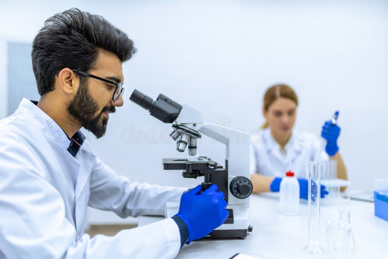ερευνητές υγειονομικής περίθαλψης που εργάζονται σε εργαστήρια επιστημών με μικροσκόπιο που εξετάζουν το μικροσκόπιο στοκ εικόνα