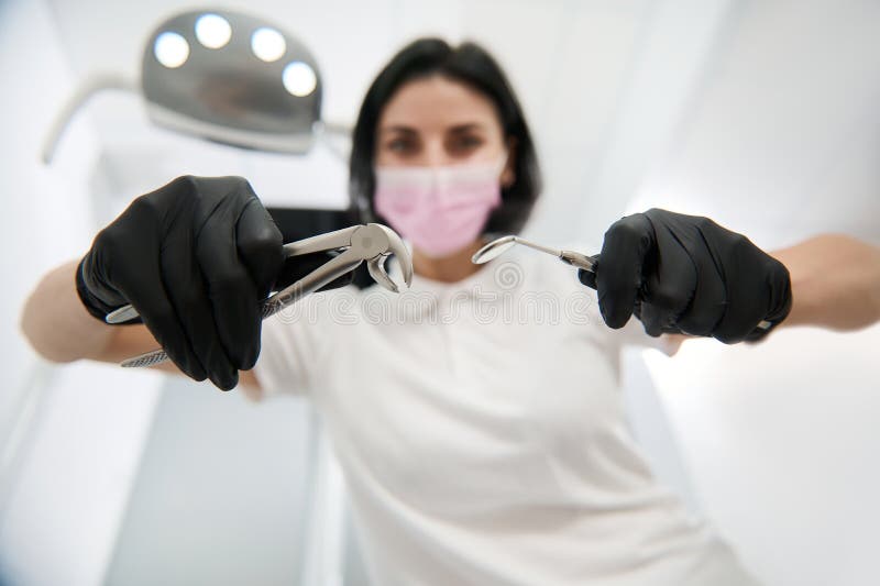 εστίαση στις λαβές εξαγωγής οδοντιατρικών οργάνων από ανοξείδωτο χάλυβα και στον οδοντιατρικό καθρέφτη στα χέρια θαμπών οδοντιάτρω στοκ φωτογραφίες