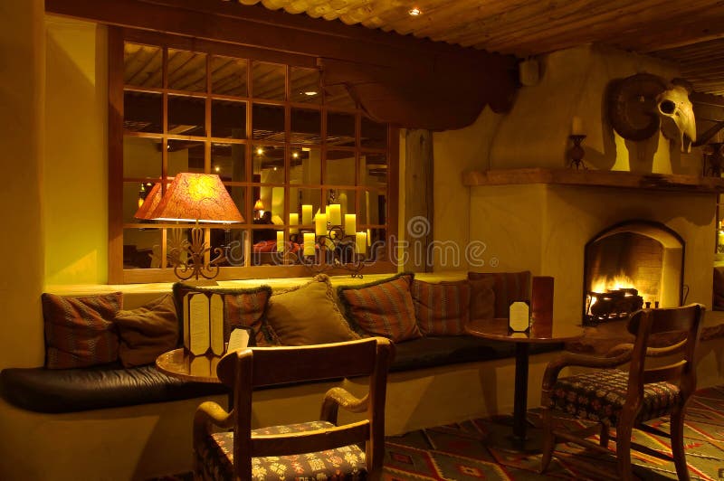 A view of a comfortable, interior hotel lounge with a fireplace, dim lighting and plenty of soft pillows on a sofa in front of a mirror. A view of a comfortable, interior hotel lounge with a fireplace, dim lighting and plenty of soft pillows on a sofa in front of a mirror.