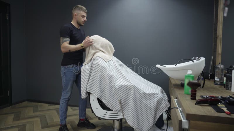 εσωτερικό σαλόνι κουρείου. λεπτό κουρέλι πετά πετσέτα πάνω από το πρόσωπο των πελατών. αρσενικός ειδικός σβήνει μαλλιά στο κεφάλι