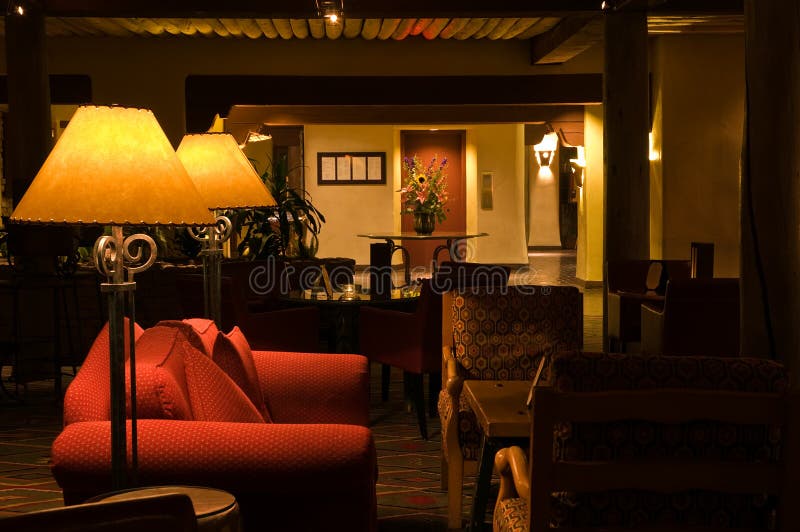 A view of a comfortable interior hotel lobby with dim lighting and plenty of soft pillows on a red sofa. A view of a comfortable interior hotel lobby with dim lighting and plenty of soft pillows on a red sofa.