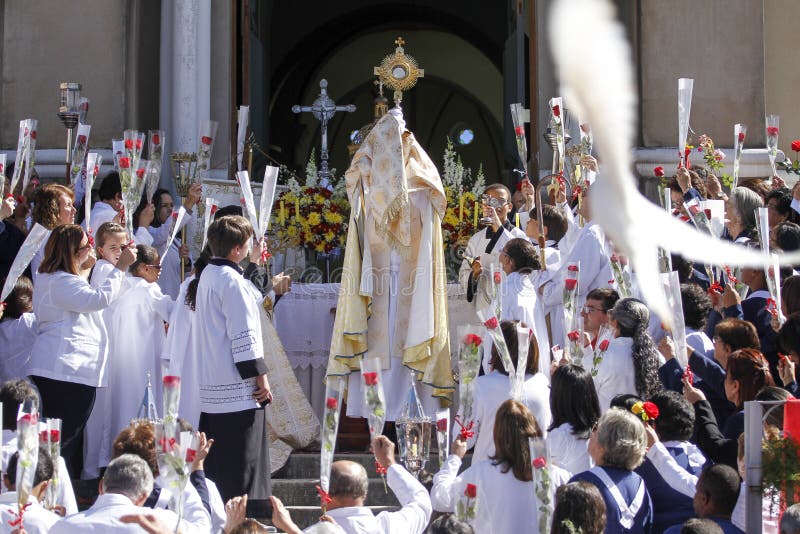 OLIVEIRA, MG / BRAZIL - 2015-06-04: Catholic celebrant blesses faithful in front of the church finishing the Corpus Christi procession. White pigeon, symbol of peace, flies in the picture of the scene. OLIVEIRA, MG / BRAZIL - 2015-06-04: Catholic celebrant blesses faithful in front of the church finishing the Corpus Christi procession. White pigeon, symbol of peace, flies in the picture of the scene.