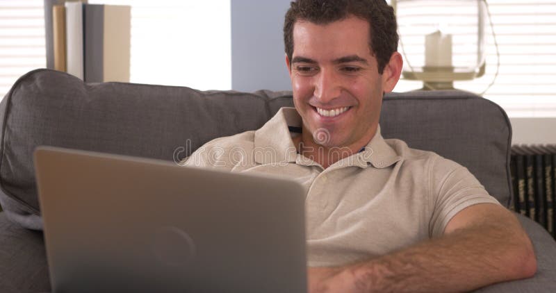 Ευτυχές άτομο που χρησιμοποιεί το lap-top στον καναπέ στοκ εικόνα Ευτυχές άτομο που χρησιμοποιεί το lap-top στον καναπέ στοκ εικόνα
