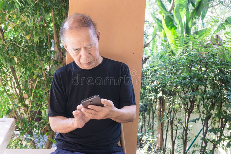 Ευτυχές ασιατικό ανώτερο άτομο που χρησιμοποιεί το κινητό τηλέφωνο στο σπίτι στοκ εικόνες Ευτυχές ασιατικό ανώτερο άτομο που χρησιμοποιεί το κινητό τηλέφωνο στο σπίτι στοκ εικόνες