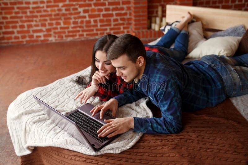 Ευτυχές ζεύγος με το lap-top που ψωνίζουν on-line στο σπίτι, κοιτάζοντας βιαστικά Διαδίκτυο στο κρεβάτι, χαμογελώντας και έχοντας στοκ φωτογραφία με δικαίωμα ελεύθερης χρήσης Ευτυχές ζεύγος με το lap-top που ψωνίζουν on-line στο σπίτι, κοιτάζοντας βιαστικά Διαδίκτυο στο κρεβάτι, χαμογελώντας και έχοντας στοκ φωτογραφία με δικαίωμα ελεύθερης χρήσης