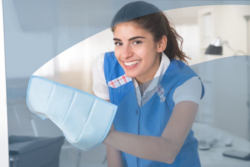 Ευτυχές θηλυκό παράθυρο γυαλιού εργαζομένων καθαρίζοντας με το κουρέλι στοκ εικόνα Ευτυχές θηλυκό παράθυρο γυαλιού εργαζομένων καθαρίζοντας με το κουρέλι στοκ εικόνα