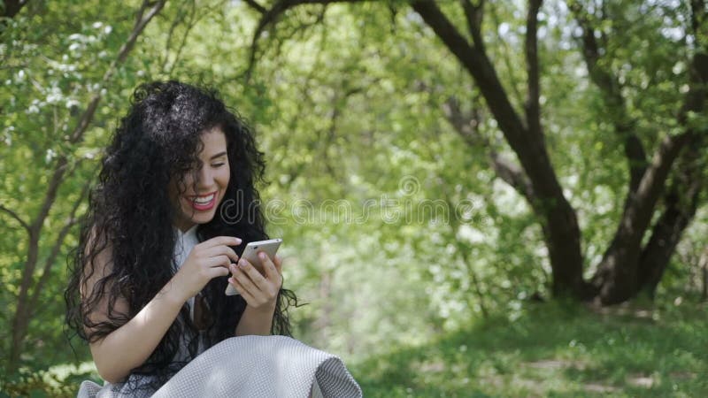 Ευτυχές μήνυμα γυναικών με τους φίλους χρησιμοποιώντας το τηλέφωνό της και χαλαρώνοντας στον κήπο