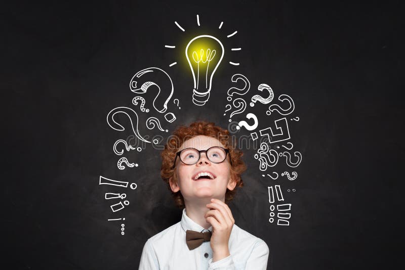 Ευτυχές παιδί που εξετάζει το lightbulb στο υπόβαθρο πινάκων Έννοια 'brainstorming' και ιδέας