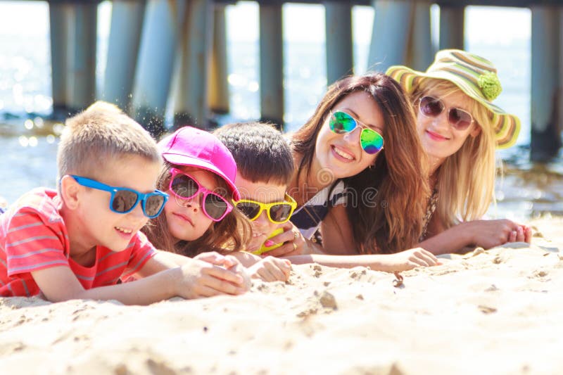 Ευτυχή παιδιά οικογενειακών γυναικών που κάνουν ηλιοθεραπεία στην παραλία