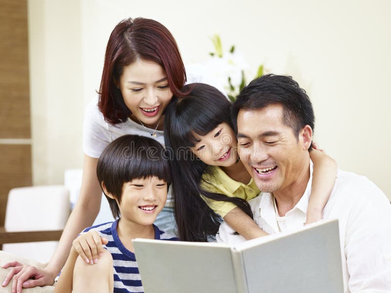 Happy asian family with two children sitting on sofa reading a book together. Happy asian family with two children sitting on sofa reading a book together.