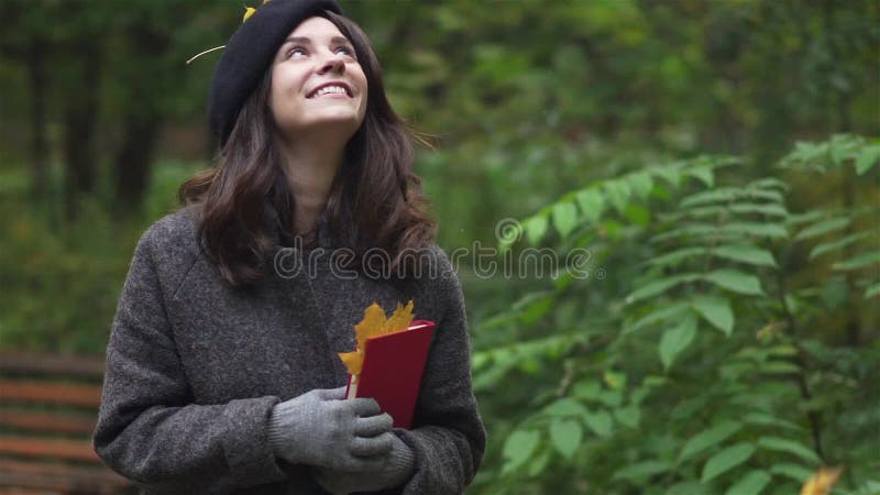 Ευτυχής γυναίκα brunette με ένα βιβλίο που χαμογελά κάτω από ένα φύλλωμα