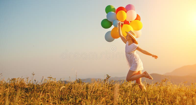 Ευτυχής γυναίκα με τα μπαλόνια στο ηλιοβασίλεμα το καλοκαίρι