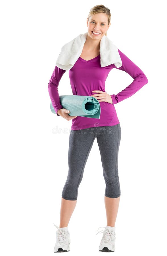 Full length portrait of happy young woman with hand on hip while holding exercise mat against white background. Full length portrait of happy young woman with hand on hip while holding exercise mat against white background