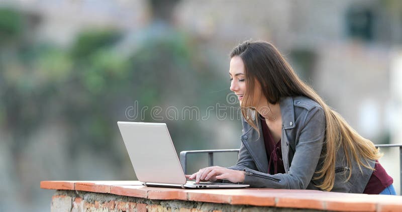 Ευτυχής δακτυλογράφηση γυναικών σε ένα lap-top σε ένα μπαλκόνι απόθεμα βίντεο