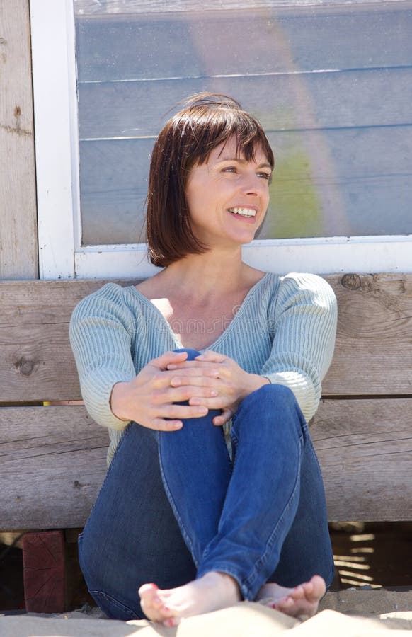 Portrait of a happy middle aged woman in jeans sitting outside. Portrait of a happy middle aged woman in jeans sitting outside