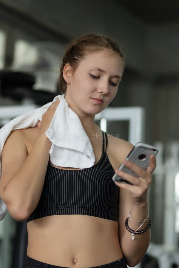 Ευτυχής νέα ελκυστική ικανότητα γυναικών που χρησιμοποιεί το smartphone που στηρίζεται στη γυμναστική κατά τη διάρκεια της άσκηση