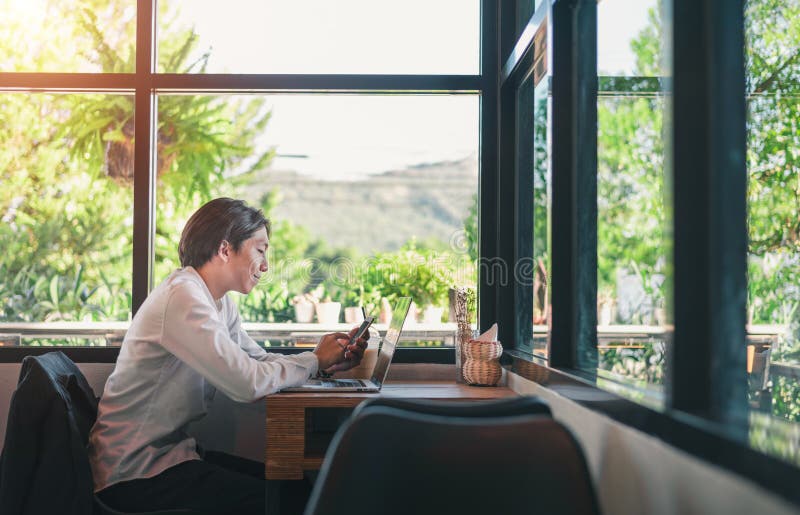 Ευτυχής νεαρός άνδρας, που φορά τα γυαλιά και που χαμογελά, όπως εργάζεται στο lap-top του για να πάρει όλη την επιχείρησή του γί στοκ εικόνα Ευτυχής νεαρός άνδρας, που φορά τα γυαλιά και που χαμογελά, όπως εργάζεται στο lap-top του για να πάρει όλη την επιχείρησή του γί στοκ εικόνα