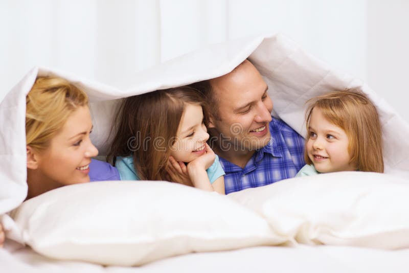 Family, children and home concept - happy family with two kids under blanket at home. Family, children and home concept - happy family with two kids under blanket at home