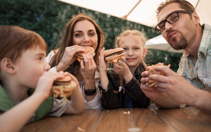 Ευτυχής οικογένεια που τρώει τα burgers που κάθονται σε έναν πίνακα σε έναν καφέ στοκ φωτογραφίες με δικαίωμα ελεύθερης χρήσης Ευτυχής οικογένεια που τρώει τα burgers που κάθονται σε έναν πίνακα σε έναν καφέ στοκ φωτογραφίες με δικαίωμα ελεύθερης χρήσης