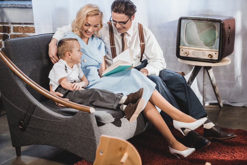 happy 1950s style family sitting on sofa and reading book together. happy 1950s style family sitting on sofa and reading book together