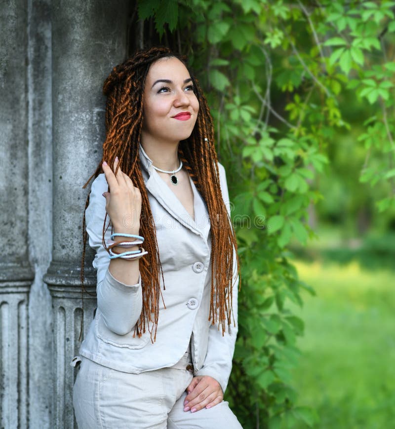 Ευτυχής τοποθέτηση κοριτσιών dreadlocks μοντέρνη κοντά στην παλαιά στήλη και τα δέντρα στοκ εικόνες με δικαίωμα ελεύθερης χρήσης Ευτυχής τοποθέτηση κοριτσιών dreadlocks μοντέρνη κοντά στην παλαιά στήλη και τα δέντρα στοκ εικόνες με δικαίωμα ελεύθερης χρήσης