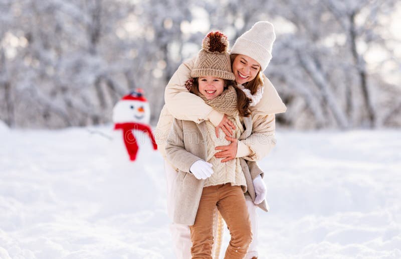 ευτυχισμένη μητέρα αγκαλιάζει την κόρη του ενώ διασκεδάζει με τον χιονισμένο καιρό έξω