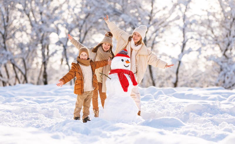 ευτυχισμένη οικογένεια μητέρα και δύο μικρά παιδιά γελάνε χαρούμενα και σηκώνουν τα χέρια ψηλά, ενώ κάνουν χιονάνθρωπο μαζί στο χε