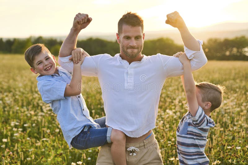 Ευτυχισμένη οικογένεια πατέρα και δύο παιδιά στο γήπεδο στο ηλιοβασίλεμα διασκεδάζοντας