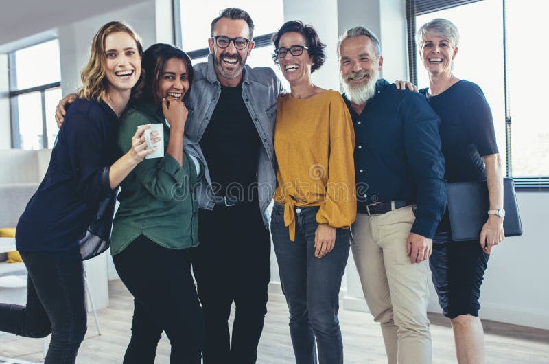 Cheerful business people standing together and laughing. Team of business professionals looking at camera and smiling. Cheerful business people standing together and laughing. Team of business professionals looking at camera and smiling