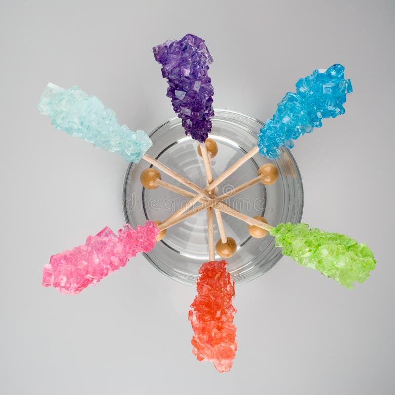 Six colors of rock sugar candy on sticks in a glass bowl on a gray background. Six colors of rock sugar candy on sticks in a glass bowl on a gray background