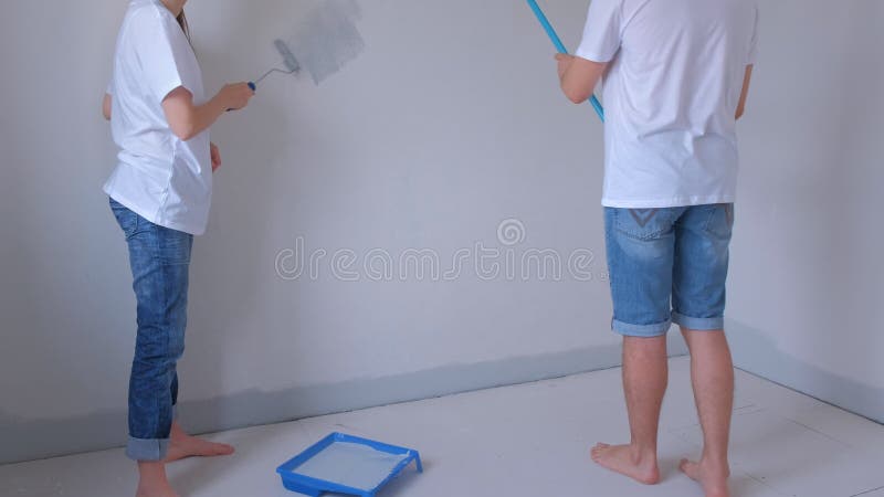 ζευγάρι νεαρός άνδρας και γυναίκα ζωγραφίζουν τον τοίχο με γκρι χρησιμοποιώντας ροδέλες μπογιάς. απόθεμα βίντεο