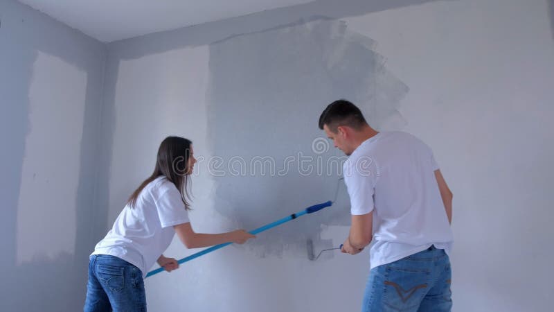 ζευγάρι νεαρός άνδρας και γυναίκα ζωγραφίζουν τον τοίχο με γκρι χρησιμοποιώντας ροδέλες μπογιάς. απόθεμα βίντεο